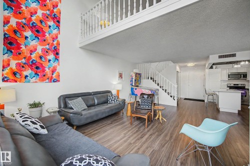 Open-concept living space featuring wood-finish flooring, a white spindle staircase, and a lofted area with a matching white spindle railing - 1205 10045 118 Street, Edmonton, AB - Indoor Photo Showing Living Room