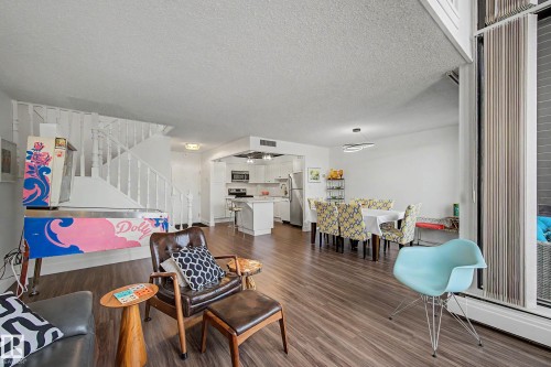 Open-concept living area featuring wood-finish flooring, white walls, and a white staircase - 1205 10045 118 Street, Edmonton, AB - Indoor