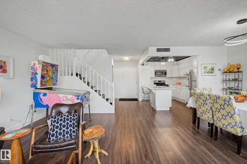 Open-concept living space featuring wood-finish flooring, a white staircase with balusters, and a contemporary kitchen - 1205 10045 118 Street, Edmonton, AB - Indoor
