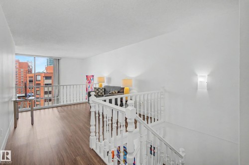 Expansive open-concept upper level featuring rich wood-finish flooring, a full wall of windows, white painted balusters, and contemporary wall sconces - 1205 10045 118 Street, Edmonton, AB - Indoor Photo Showing Other Room
