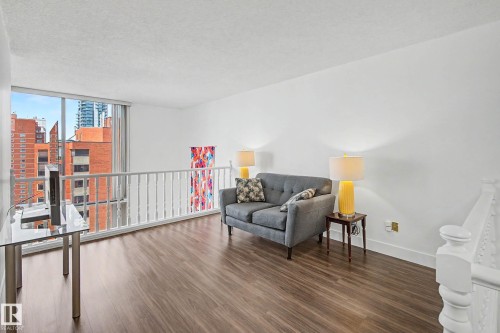 Open-concept living space with expansive windows, wood-finish flooring, a white spindle railing, and bright white walls - 1205 10045 118 Street, Edmonton, AB - Indoor Photo Showing Other Room