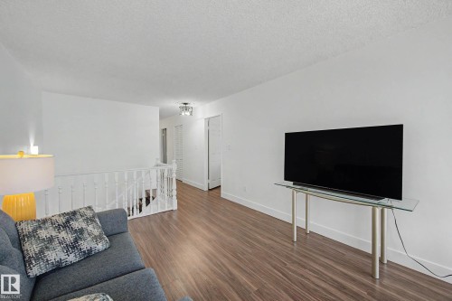 Living area featuring wood-finish flooring, white walls, a white staircase railing, and a modern flush-mount ceiling light fixture - 1205 10045 118 Street, Edmonton, AB - Indoor Photo Showing Living Room
