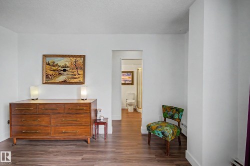 Wood-finish flooring throughout, bright white walls, and a recessed doorway leading to a bathroom - 1205 10045 118 Street, Edmonton, AB - Indoor Photo Showing Other Room