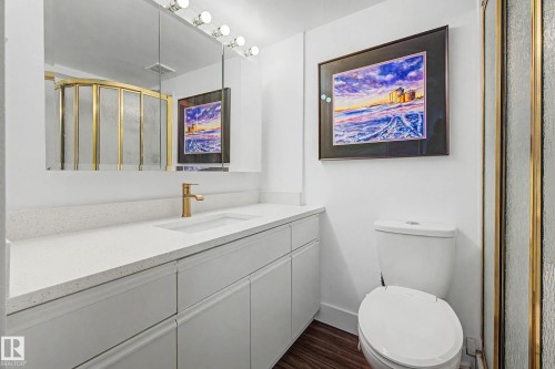 Bathroom featuring a gold-toned framed shower enclosure, a vanity with a white countertop and integrated sink, a gold-toned faucet, and a large mirrored medicine cabinet with overhead lighting - 1205 10045 118 Street, Edmonton, AB - Indoor Photo Showing Bathroom