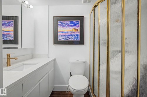 Bathroom featuring a white vanity with an integrated sink, a gold-toned faucet, and an enclosed shower with gold-toned framing - 1205 10045 118 Street, Edmonton, AB - Indoor Photo Showing Bathroom
