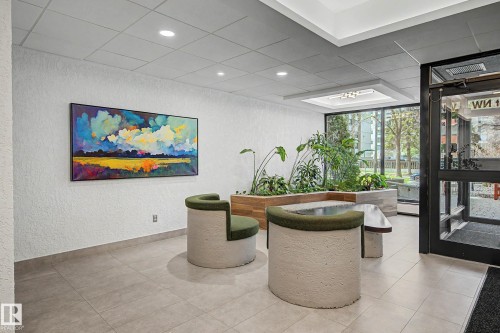 Contemporary lobby area featuring light tile flooring, white textured walls, recessed ceiling lighting, and a large decorative planter with mature greenery - 1205 10045 118 Street, Edmonton, AB - Indoor Photo Showing Other Room