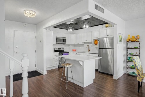 Updated kitchen featuring white shaker cabinetry, stainless steel appliances, a center island with seating, white countertops, and wood-finish flooring - 1205 10045 118 Street, Edmonton, AB - Indoor Photo Showing Kitchen