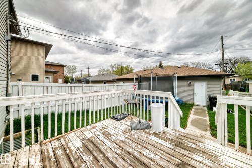 Rear yard featuring a wood deck with white railings, a concrete walkway, and a detached building with horizontal siding and a brown shingle roof - 1 12833 123 Street, Edmonton, AB - Outdoor With Deck Patio Veranda With Exterior