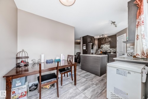 Open-concept kitchen and dining area featuring dark wood-finish cabinetry, a central island with a light-toned countertop, and patterned tile backsplash - 1 12833 123 Street, Edmonton, AB - Indoor