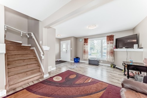 Bright open-concept living space featuring wood-finish flooring, a large window, and light neutral walls - 1 12833 123 Street, Edmonton, AB - Indoor
