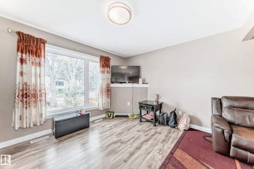 Living area featuring wood-finish flooring, a large window, neutral wall tones, a ceiling-mounted light fixture, and white baseboards - 1 12833 123 Street, Edmonton, AB - Indoor