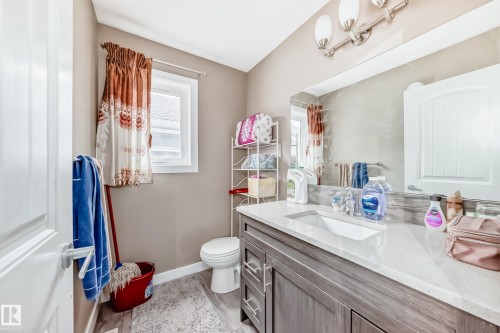 Bathroom featuring a single vanity with stone-look countertop, integrated sink, and wood-finish cabinetry - 1 12833 123 Street, Edmonton, AB - Indoor Photo Showing Bathroom