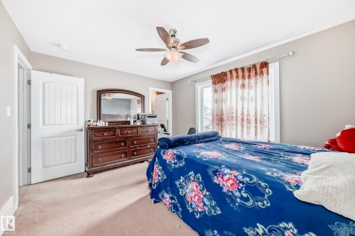 Carpeted room featuring a ceiling fan with light fixture, a window with decorative curtains, and a white paneled door - 1 12833 123 Street, Edmonton, AB - Indoor Photo Showing Bedroom