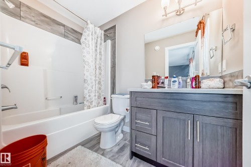 Bathroom featuring a grey wood-finish vanity with a light countertop, a built-in mirror, and a three-light fixture - 1 12833 123 Street, Edmonton, AB - Indoor Photo Showing Bathroom