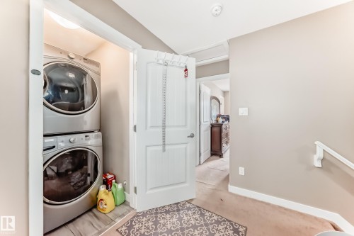 Dedicated laundry closet featuring a stacked washer and dryer, recessed lighting, and wood-finish flooring - 1 12833 123 Street, Edmonton, AB - Indoor Photo Showing Laundry Room