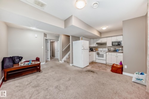 Open-concept living space featuring a compact kitchen with white cabinetry, a built-in microwave, and a white appliance suite - 1 12833 123 Street, Edmonton, AB - Indoor Photo Showing Kitchen