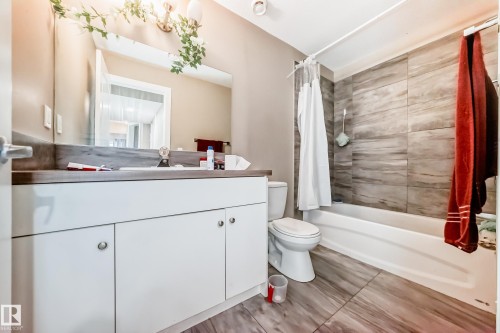 Bathroom featuring a white vanity with integrated sink, a large wall-mounted mirror, and a combination tub/shower with full-height tile surround - 1 12833 123 Street, Edmonton, AB - Indoor Photo Showing Bathroom