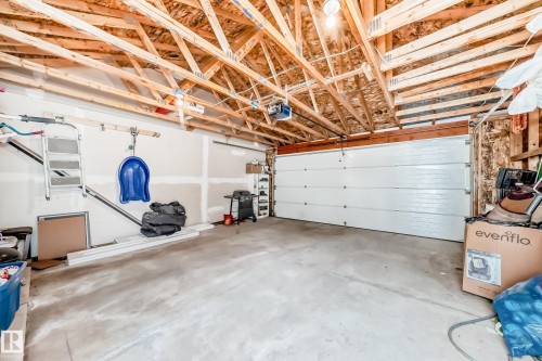 Spacious garage featuring exposed wood rafters, a concrete floor, an overhead garage door with an opener, and interior drywall finishing - 1 12833 123 Street, Edmonton, AB - Indoor Photo Showing Garage