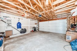 Spacious garage featuring exposed wood rafters, a concrete floor, an overhead garage door with an opener, and interior drywall finishing - 