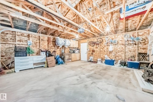 Spacious garage featuring exposed wood framing, concrete flooring, and ample overhead lighting - 1 12833 123 Street, Edmonton, AB - Indoor Photo Showing Garage