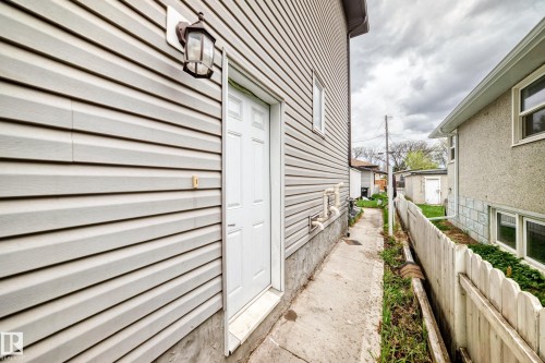 Light-colored vinyl siding exterior featuring a white paneled door and an exterior wall lantern - 1 12833 123 Street, Edmonton, AB - Outdoor