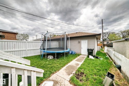 Fenced backyard featuring a detached structure with light grey siding and a brown shingled roof, a concrete pathway, and a white picket fence - 1 12833 123 Street, Edmonton, AB - Outdoor With Exterior