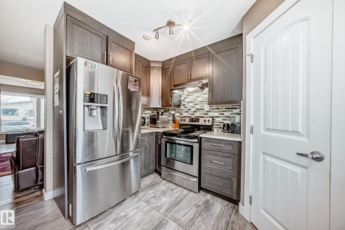 Modern kitchen with rich wood-finish cabinetry, stainless steel appliances, and a mosaic tile backsplash - 1 12833 123 Street, Edmonton, AB - Indoor Photo Showing Kitchen With Upgraded Kitchen