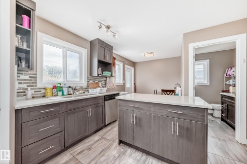 Kitchen featuring wood-finish cabinetry, light countertops, mosaic tile backsplash, and stainless steel appliances - 1 12833 123 Street, Edmonton, AB - Indoor Photo Showing Kitchen