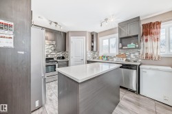 Kitchen featuring a central island with a solid surface countertop, wood-finish flooring, full-height cabinetry, stainless steel appliances, and a tiled backsplash - 
