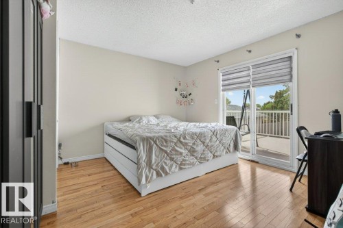 Hardwood flooring throughout this room featuring a sliding glass door providing access to an exterior deck with white railing - 157 Kiniski Crescent, Edmonton, AB - Indoor Photo Showing Bedroom