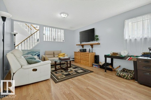 Spacious room featuring wood-finish flooring, light blue wall paint, a built-in shelf, and a window with sheer curtains - 157 Kiniski Crescent, Edmonton, AB - Indoor Photo Showing Living Room