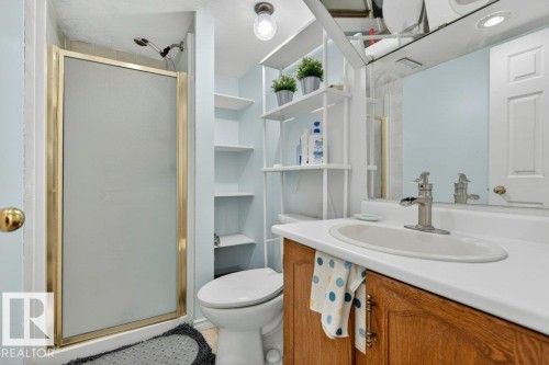 Bathroom featuring a brass-framed shower enclosure, wood-finish vanity with an integrated sink, satin nickel faucet, and a wall-mounted mirror - 157 Kiniski Crescent, Edmonton, AB - Indoor Photo Showing Bathroom