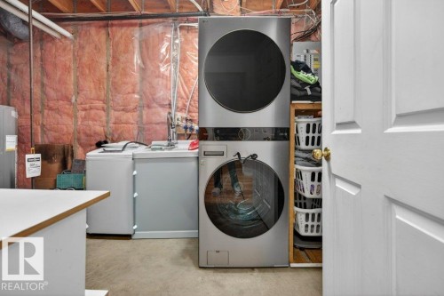 Dedicated laundry area featuring a stacked washer and dryer unit, additional utility sink, and durable concrete flooring - 157 Kiniski Crescent, Edmonton, AB - Indoor Photo Showing Laundry Room
