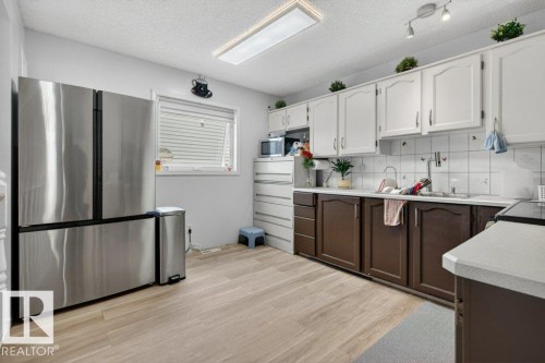 Kitchen with wood-finish flooring, stainless steel French door refrigerator, white upper cabinetry, and brown lower cabinetry - 157 Kiniski Crescent, Edmonton, AB - Indoor Photo Showing Kitchen