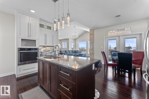 Well-appointed kitchen featuring hardwood floors, white cabinetry, integrated oven, a granite-topped island with a sink, and pendant lighting - 1513 Horseshoe Bay Estates, Cold Lake, AB - Indoor