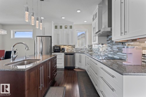 The property features a kitchen with dark hardwood flooring, an island with a sink and granite countertop, and white cabinetry with stainless steel appliances - 1513 Horseshoe Bay Estates, Cold Lake, AB - Indoor Photo Showing Kitchen With Upgraded Kitchen