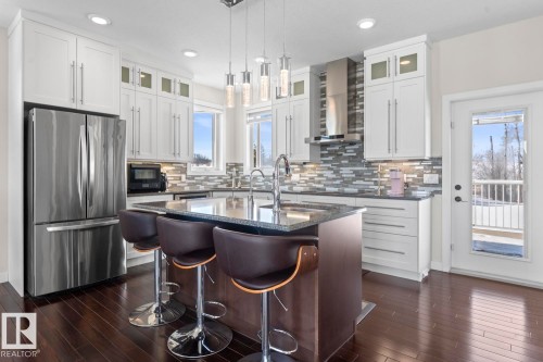 The kitchen features dark wood floors, white cabinetry, a stainless steel refrigerator, and a kitchen island with a dark countertop and pendant lighting - 1513 Horseshoe Bay Estates, Cold Lake, AB - Indoor