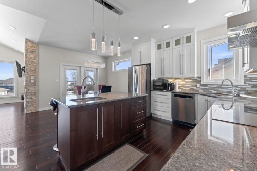 The kitchen features dark wood flooring, white cabinetry, stainless steel appliances, and an island with a sink and pendant lighting - 1513 Horseshoe Bay Estates, Cold Lake, AB - Indoor Photo Showing Kitchen With Upgraded Kitchen
