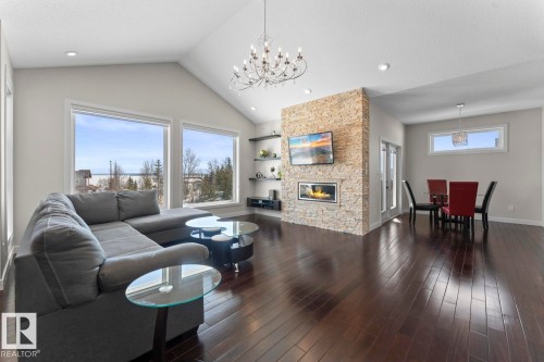 This inviting living space features dark hardwood floors, a vaulted ceiling with a chandelier, and large windows providing abundant natural light - 1513 Horseshoe Bay Estates, Cold Lake, AB - Indoor Photo Showing Living Room With Fireplace