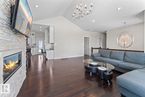 The living area features dark hardwood floors, a stone-faced fireplace with a television mounted above, and a vaulted ceiling with a chandelier - 1513 Horseshoe Bay Estates, Cold Lake, AB - Indoor Photo Showing Living Room With Fireplace