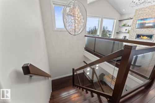 The property features stairs with dark wood treads and a glass railing system, a white wall, and windows providing natural light - 1513 Horseshoe Bay Estates, Cold Lake, AB - Indoor Photo Showing Other Room With Fireplace