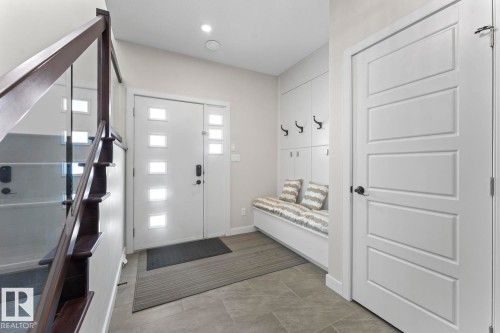 The property features a bright entryway with a modern front door, a built-in storage bench with coat hooks, and a staircase with a glass railing and dark wood accents - 1513 Horseshoe Bay Estates, Cold Lake, AB - Indoor Photo Showing Other Room