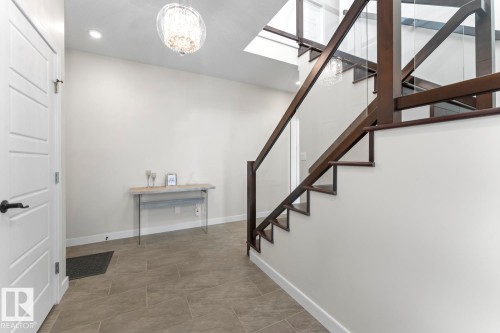 Entryway featuring tiled flooring, a contemporary staircase with glass paneling, and a stylish chandelier - 1513 Horseshoe Bay Estates, Cold Lake, AB - Indoor Photo Showing Other Room