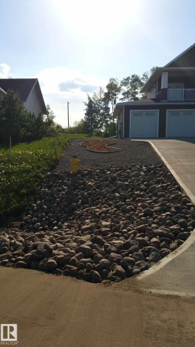 The property features a dark-colored exterior with white garage doors and a paved driveway - 1513 Horseshoe Bay Estates, Cold Lake, AB - Outdoor