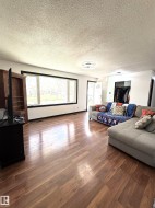 Spacious living area featuring wood-finish flooring, a large picture window with black trim, and white walls - 
