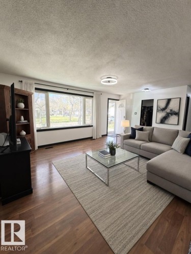 Living area featuring wood-finish flooring, a large picture window with black trim, and a contemporary ceiling light fixture - 45 Lambert Crescent, St. Albert, AB - Indoor Photo Showing Living Room