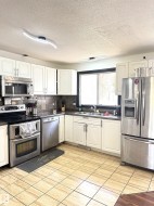 Kitchen featuring white cabinetry, stainless steel appliances, dark countertops, and a tiled backsplash - 