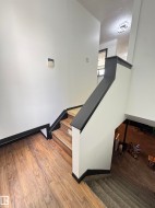 Interior staircase featuring wood-finish flooring, white walls, and dark trim - 