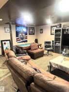 Recessed lighting illuminates a spacious room featuring a pool table, wall-mounted display, and carpeted flooring - 