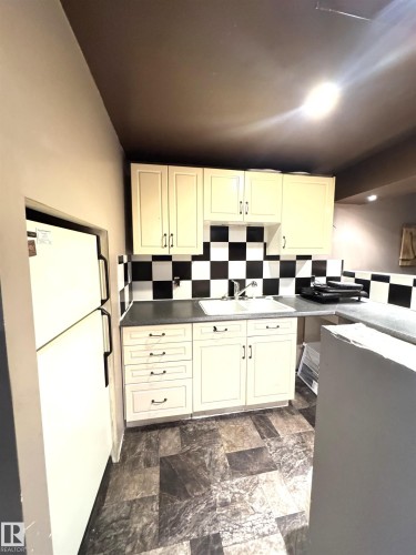 Kitchen featuring cream cabinetry, checkerboard backsplash, a double basin sink, stone-finish countertops, and patterned vinyl flooring - 45 Lambert Crescent, St. Albert, AB - Indoor Photo Showing Kitchen